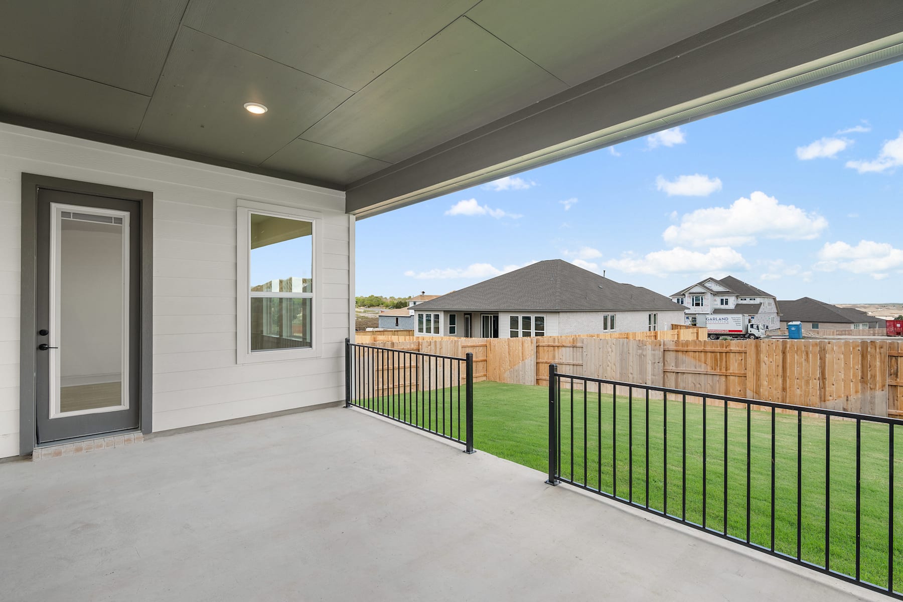 A spacious outdoor patio with a lush green lawn, surrounded by a wooden fence and overlooking a scenic landscape with mountains in the distance.