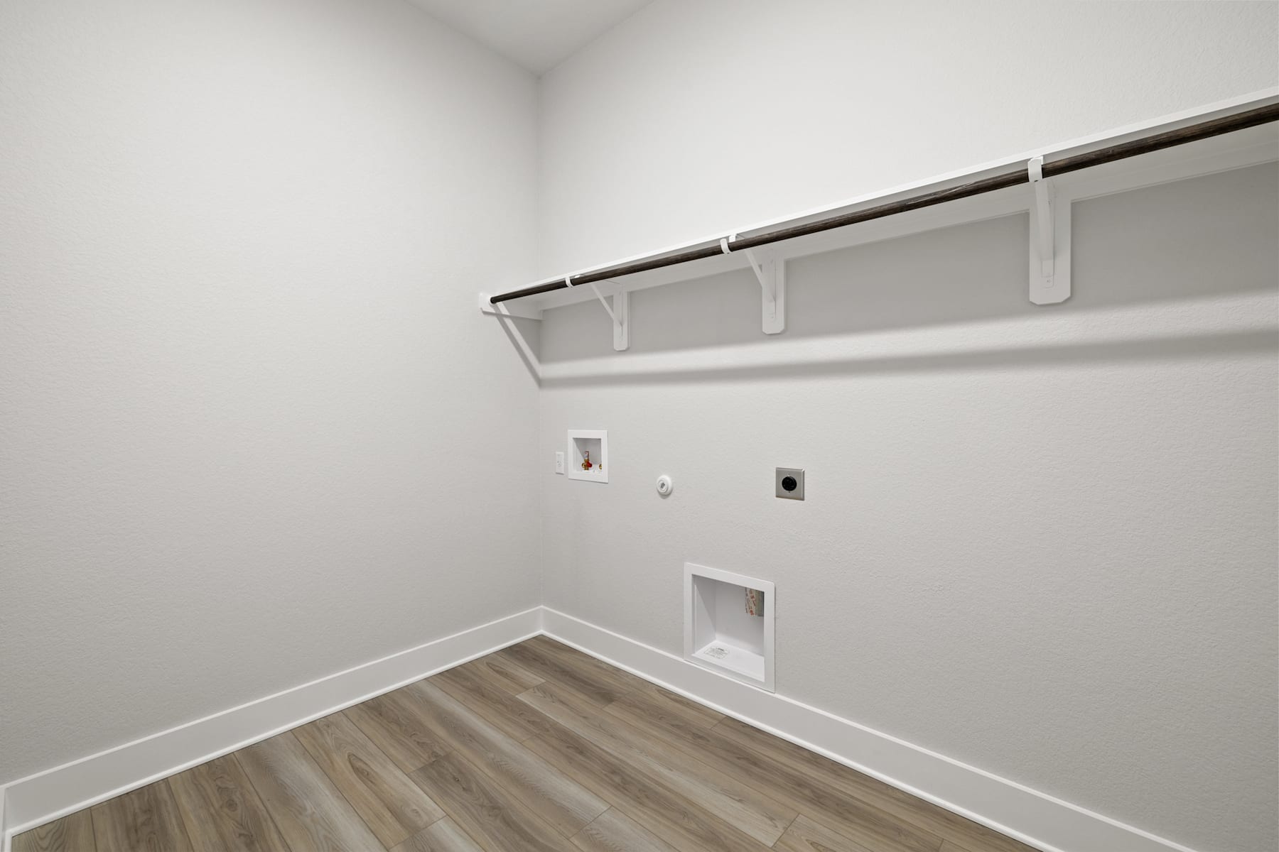 A minimalist corner of a room with a white wall, a wooden floor, and a white shelf with a rod for hanging clothes.
