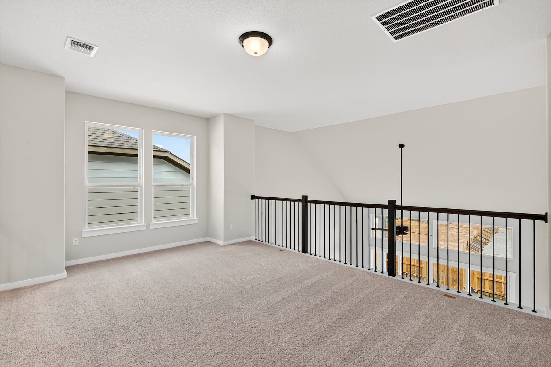 A spacious, well-lit room with a balcony overlooking the exterior, featuring a carpeted floor, a ceiling light fixture, and a metal railing.