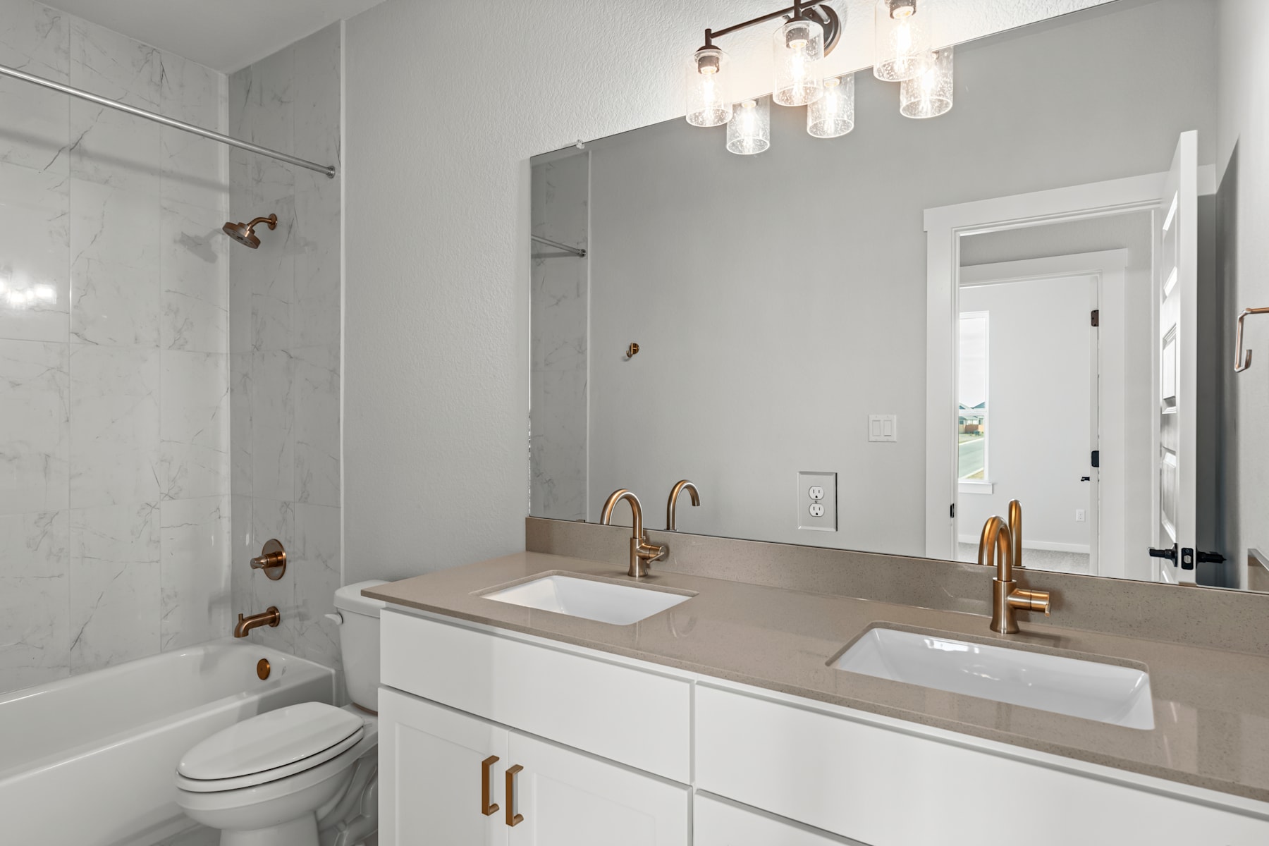 A modern, minimalist bathroom with a white vanity, dual sinks, and a large mirror illuminated by a stylish light fixture.