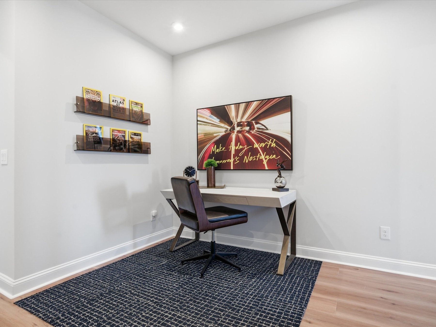 A modern home office space with a white desk, a colorful abstract artwork on the wall, and shelves displaying various items.