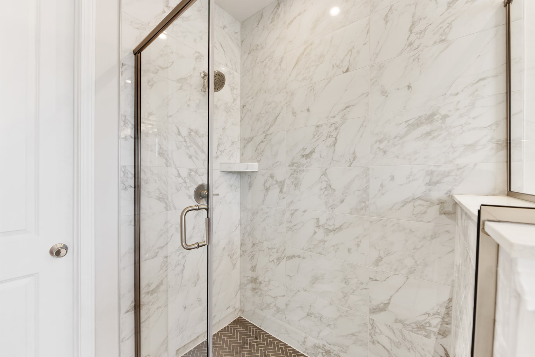 A modern, minimalist bathroom with a glass shower enclosure and white marble walls, creating a sleek and elegant aesthetic.