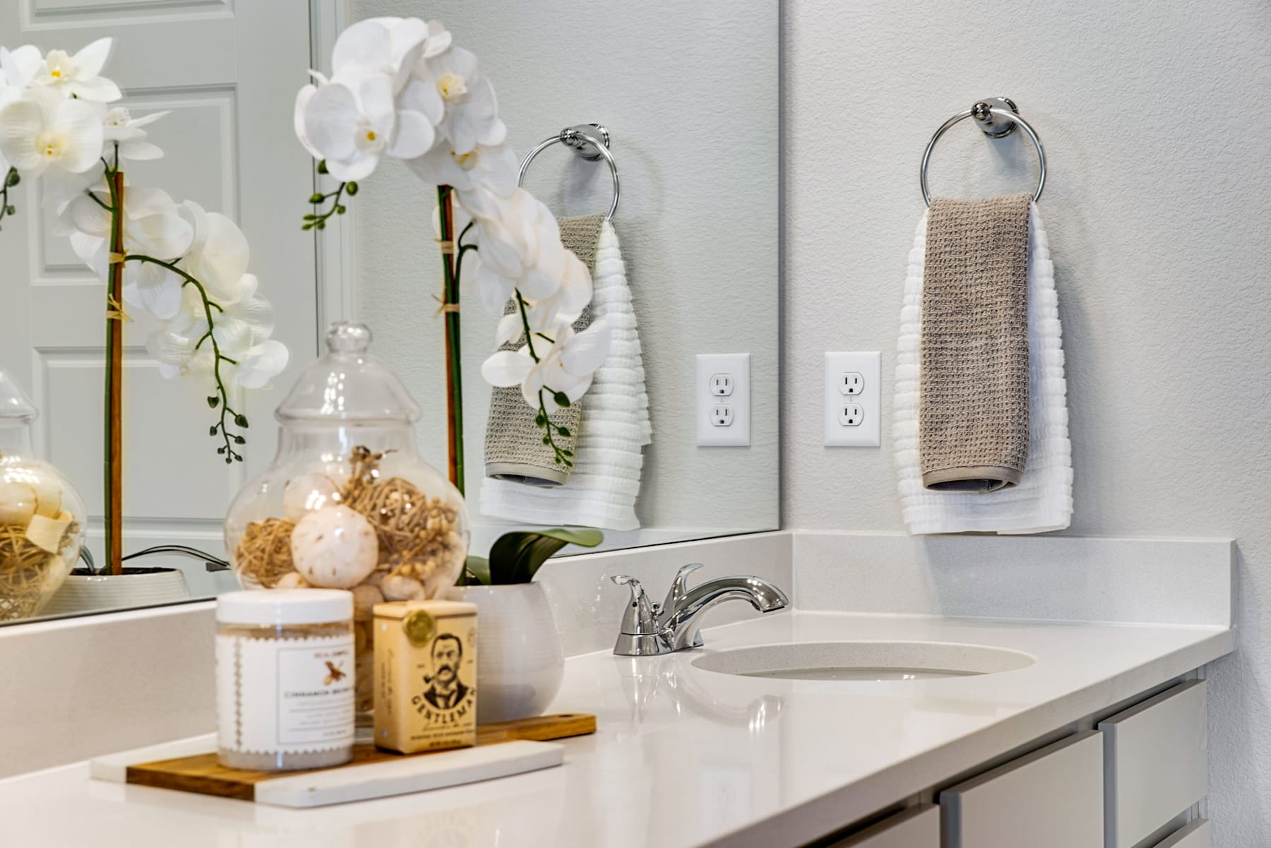 A well-decorated bathroom with white orchids, towels, and various decorative items on the vanity.