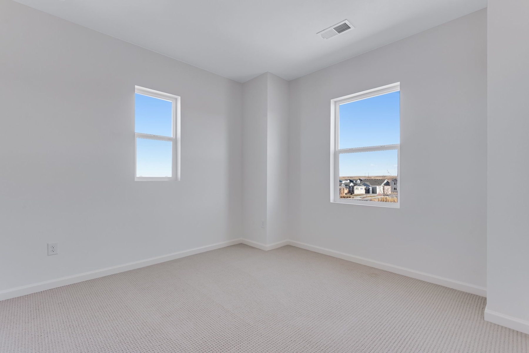 An empty, bright room with white walls and windows overlooking a residential neighborhood in the background.