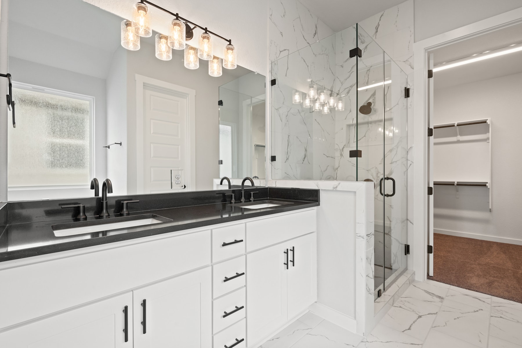 A modern, well-lit bathroom with white cabinets, a black countertop, and a glass-enclosed shower area. The room features a sleek and minimalist design with a touch of elegance.
