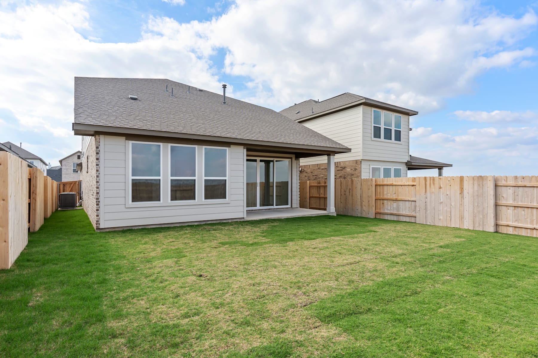 A modern two-story house with a well-manicured lawn and a wooden fence in the foreground, set against a backdrop of a partly cloudy sky.