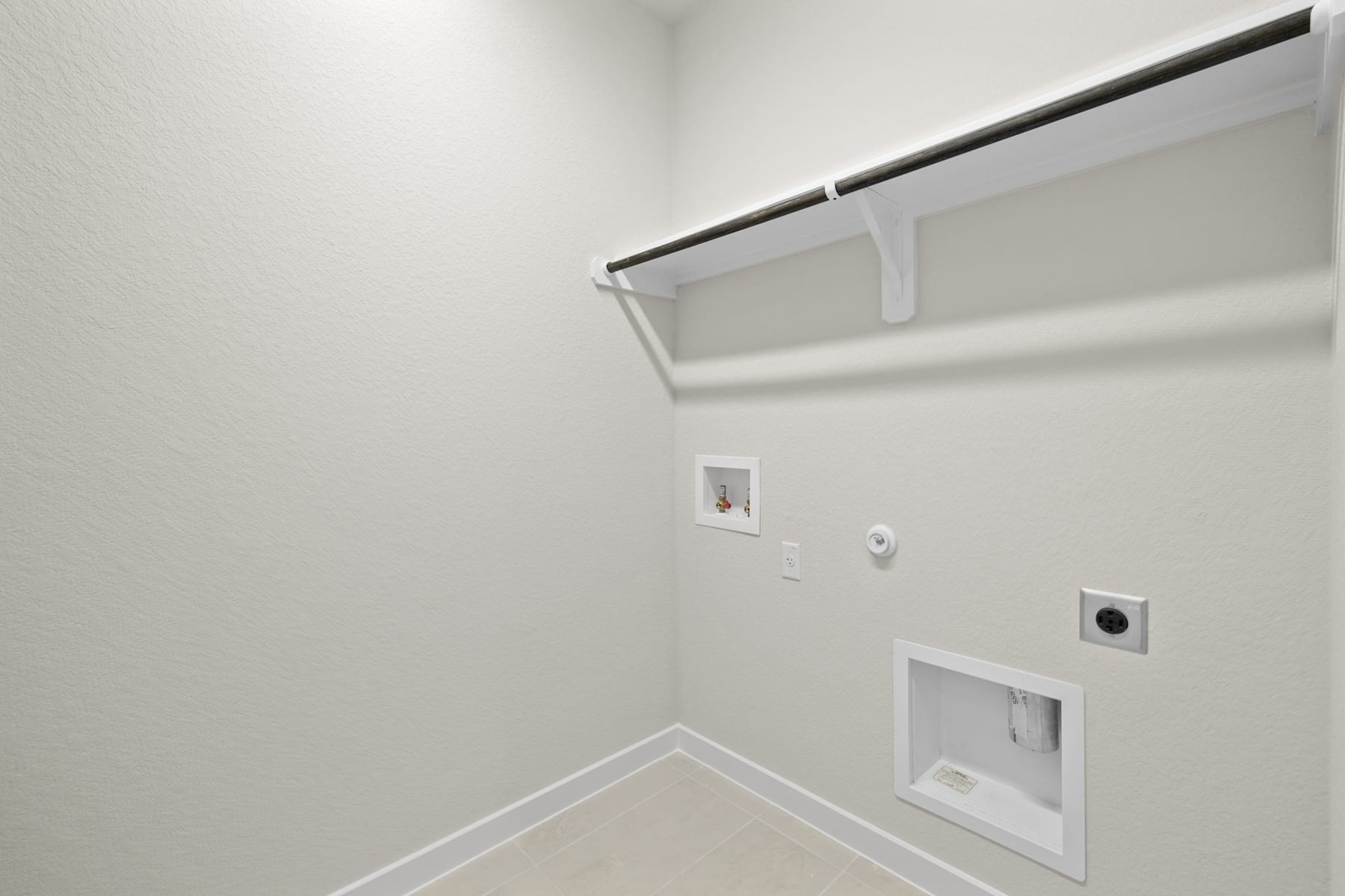 A minimalist, white-walled room with a closet rod and shelving system, along with electrical outlets and a light switch visible on the wall.
