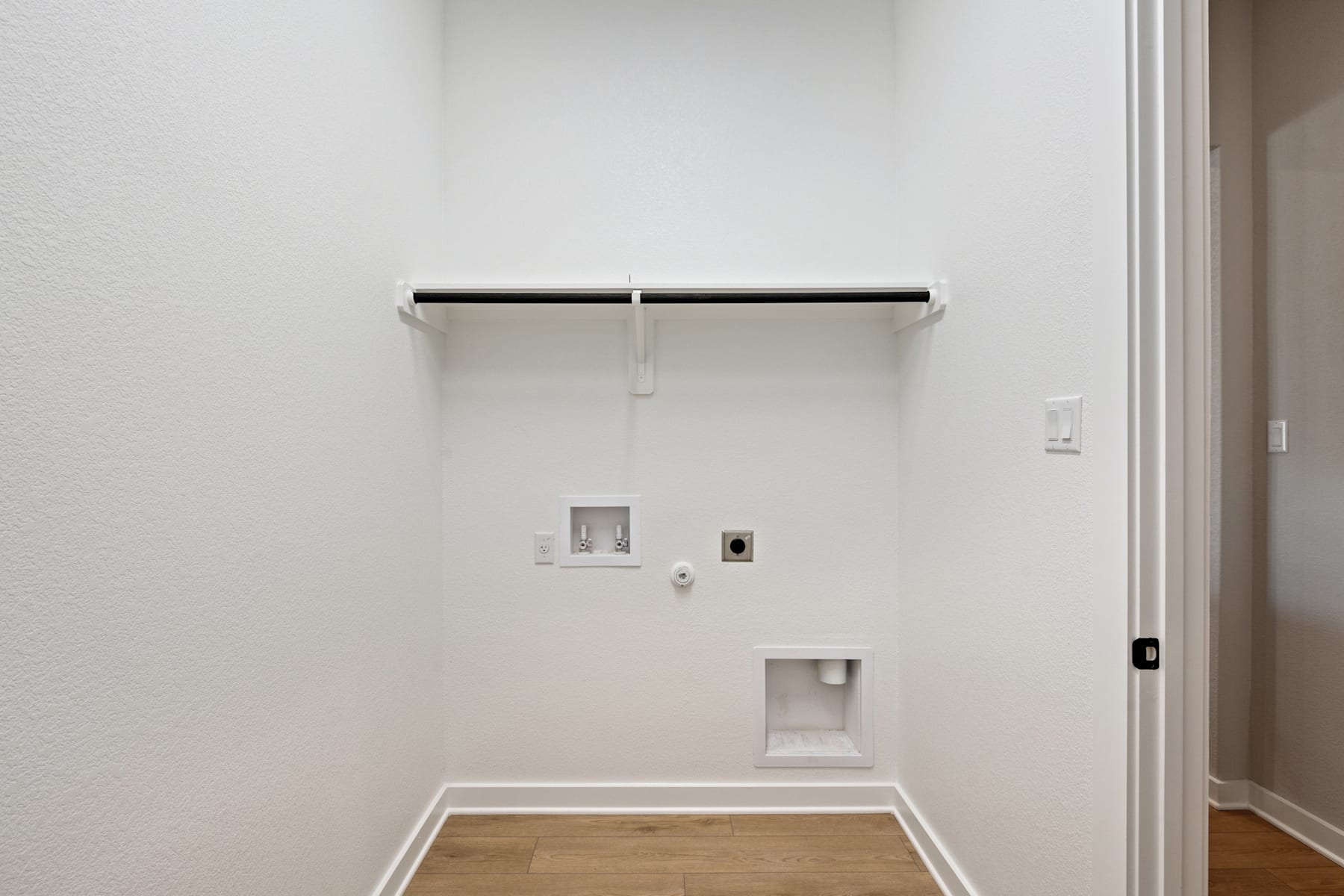 A simple, minimalist interior with a white wall, a hanging rod, and a wooden floor.