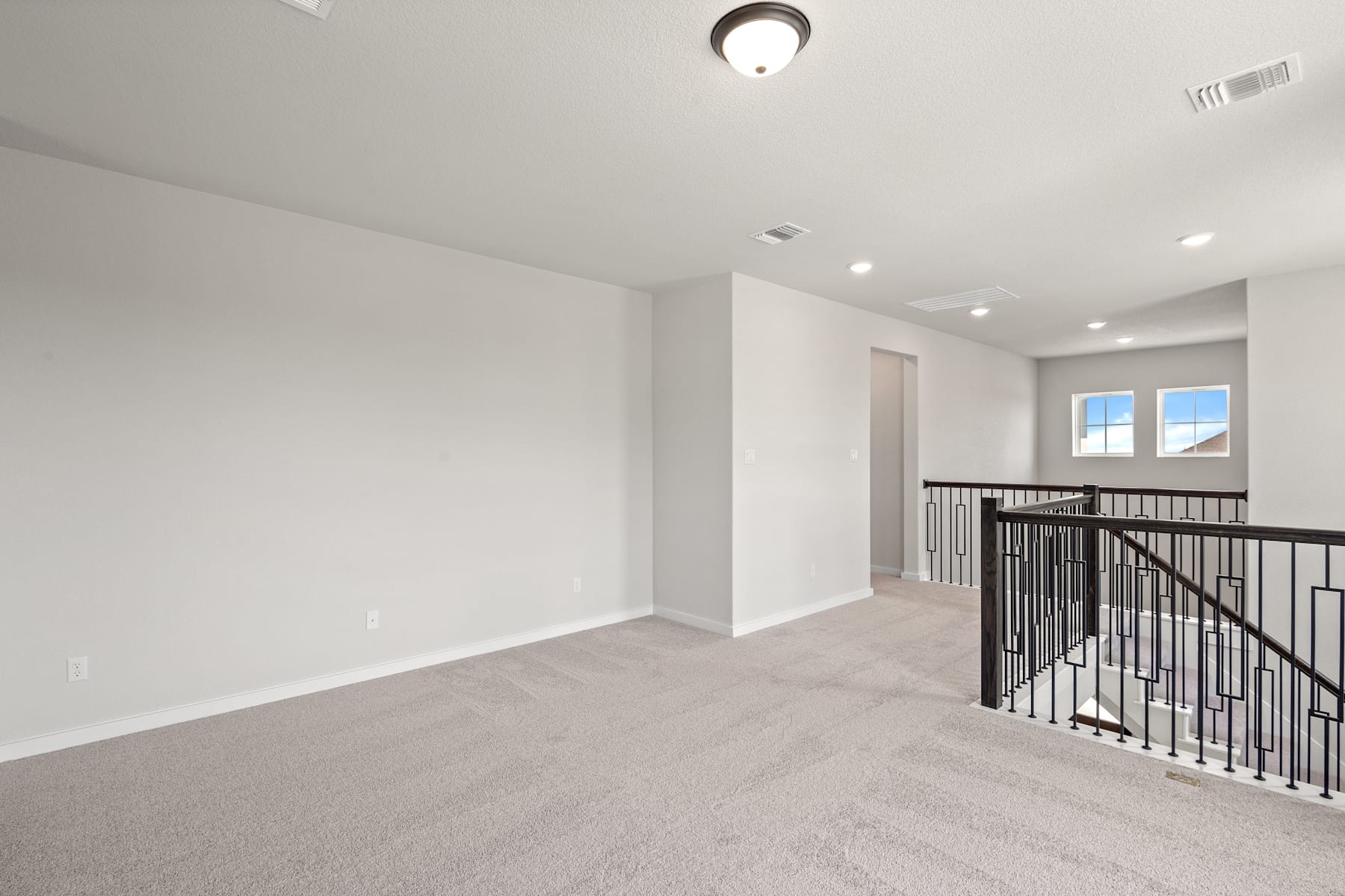 A spacious, well-lit room with a carpeted floor, a railing, and a ceiling light fixture.