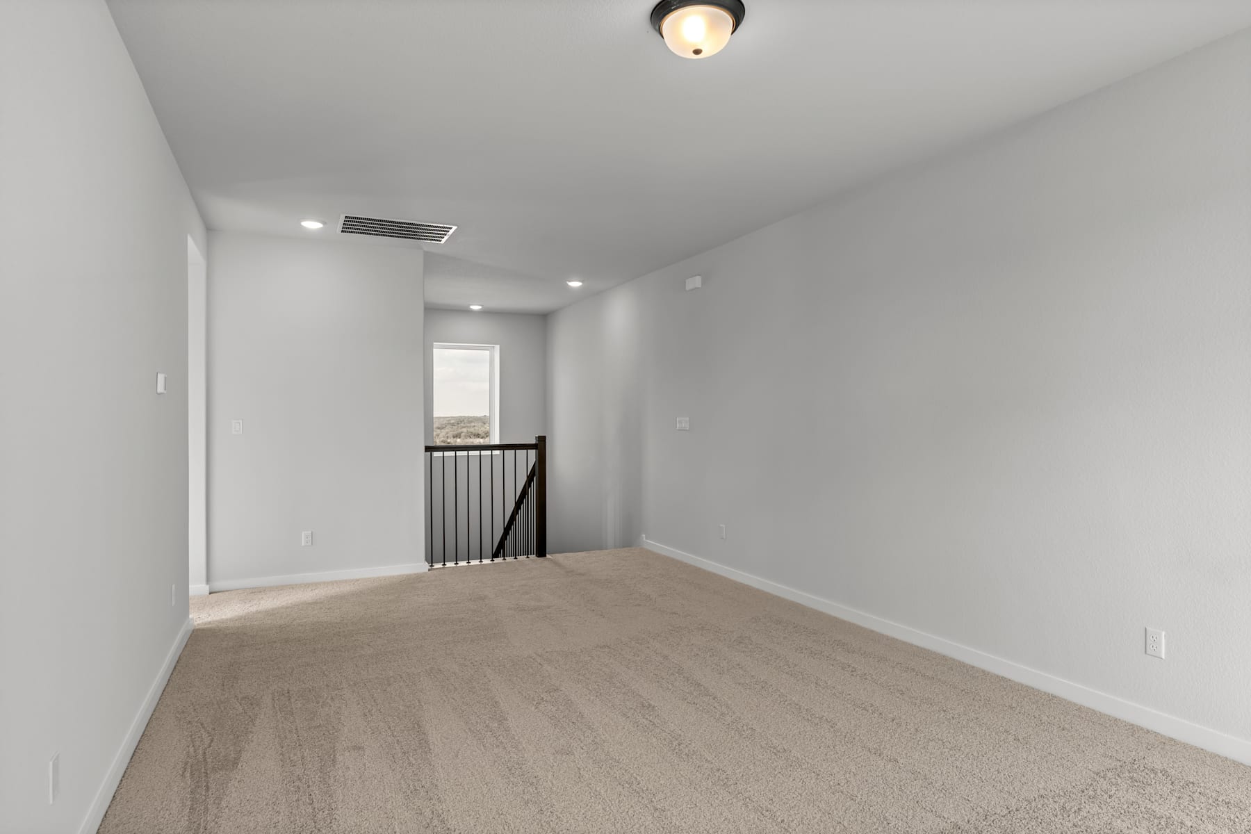 A spacious, minimalist room with white walls, a hardwood floor, and a ceiling light fixture.