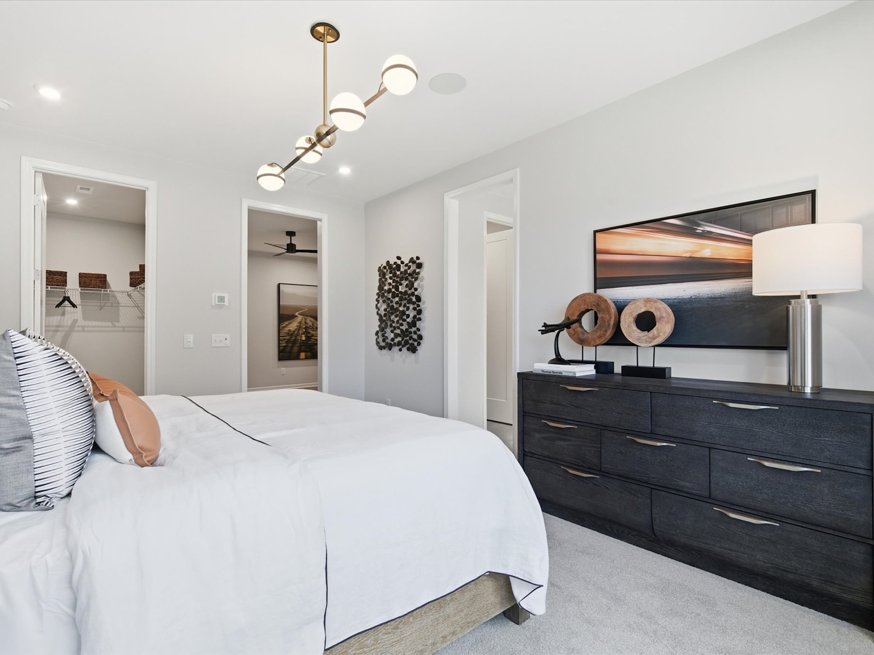 A modern and stylish bedroom with a large bed, a dresser with drawers, and various decorative elements such as artwork and lighting fixtures.