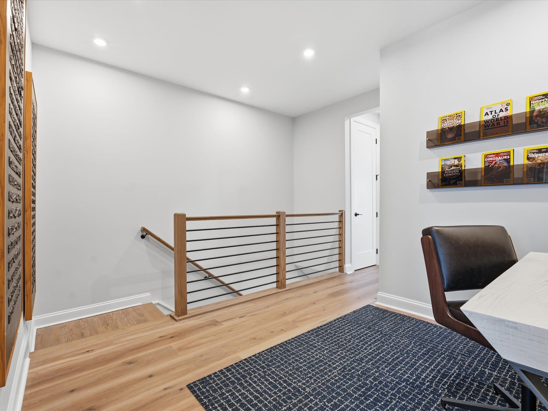 A modern, minimalist hallway with wooden floors, a railing, and framed artwork on the walls.