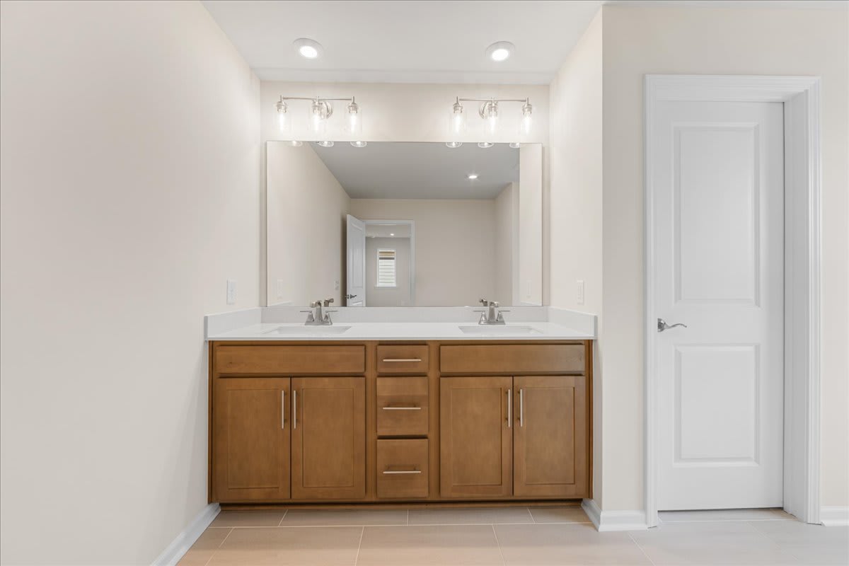 A modern bathroom vanity with wooden cabinets and a white marble countertop, set against a bright and airy background with white walls and recessed lighting.