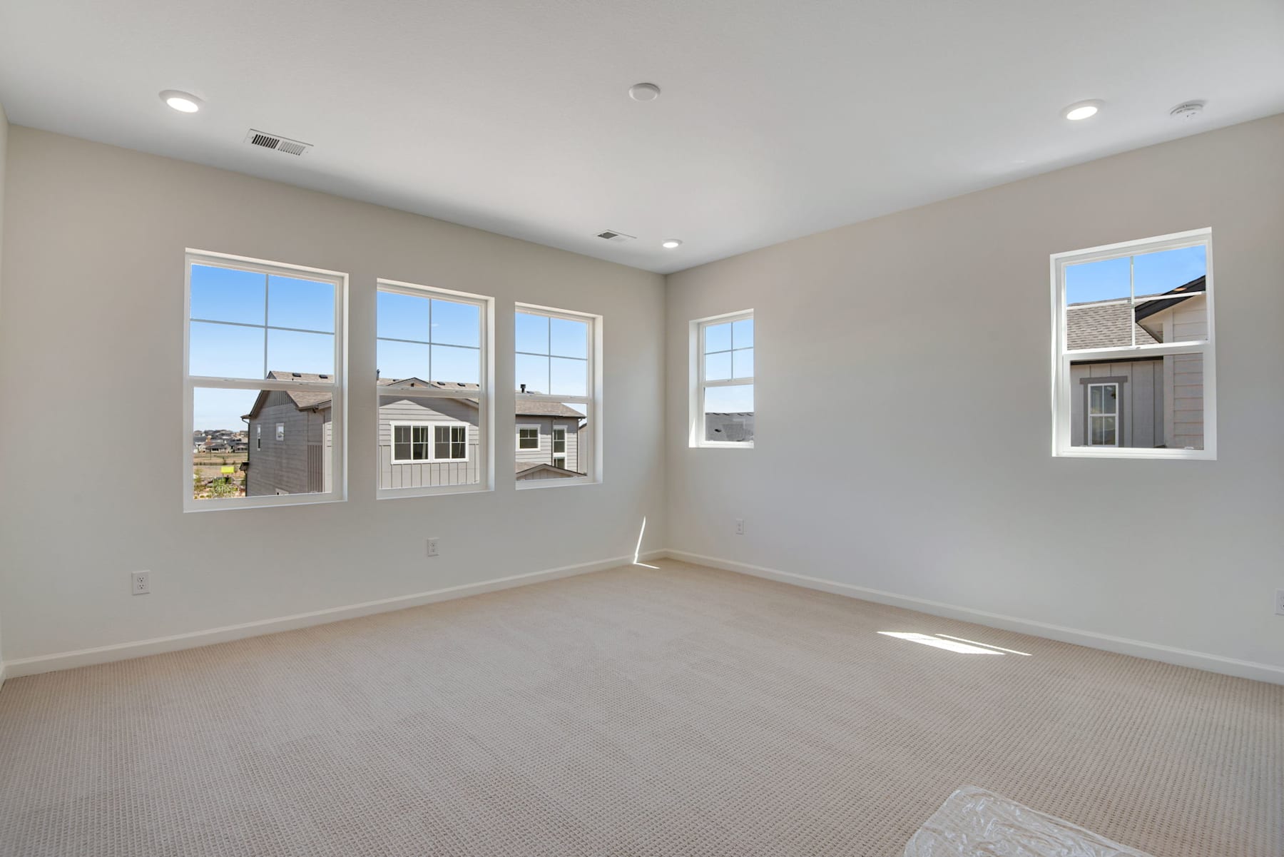 A spacious, well-lit room with large windows overlooking a residential neighborhood in the background.