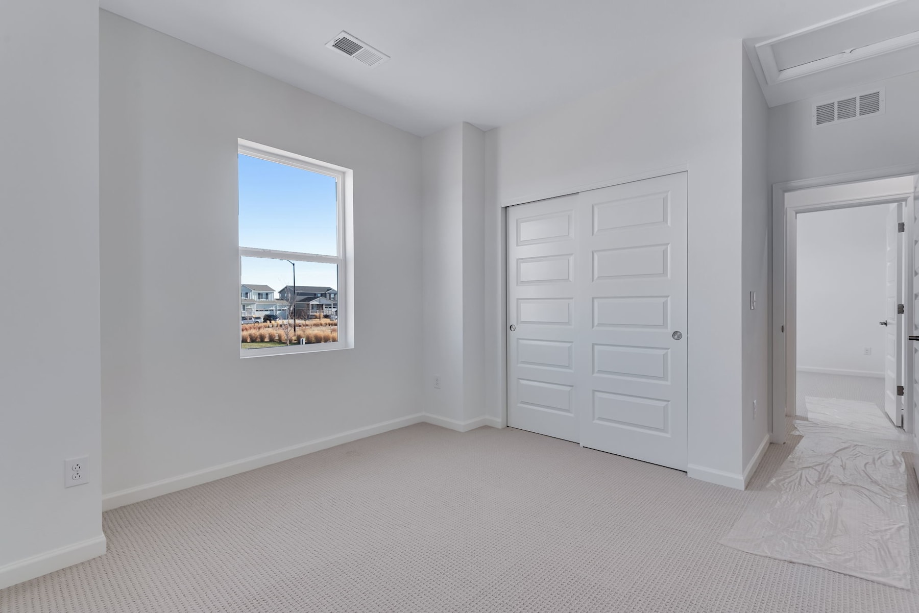A spacious, well-lit room with white walls, a large window, and a closed door leading to another area.
