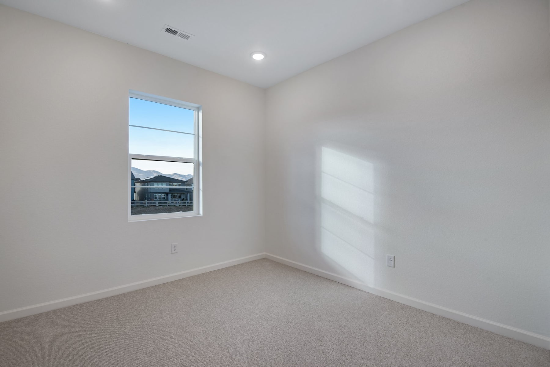 A bright, empty room with a large window overlooking a residential neighborhood in the background.