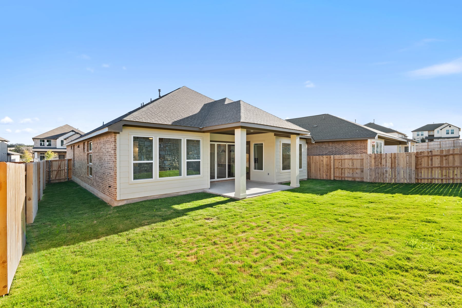 A well-manicured lawn surrounds a modern, single-story house with a peaked roof and large windows, set against a clear blue sky with some clouds.