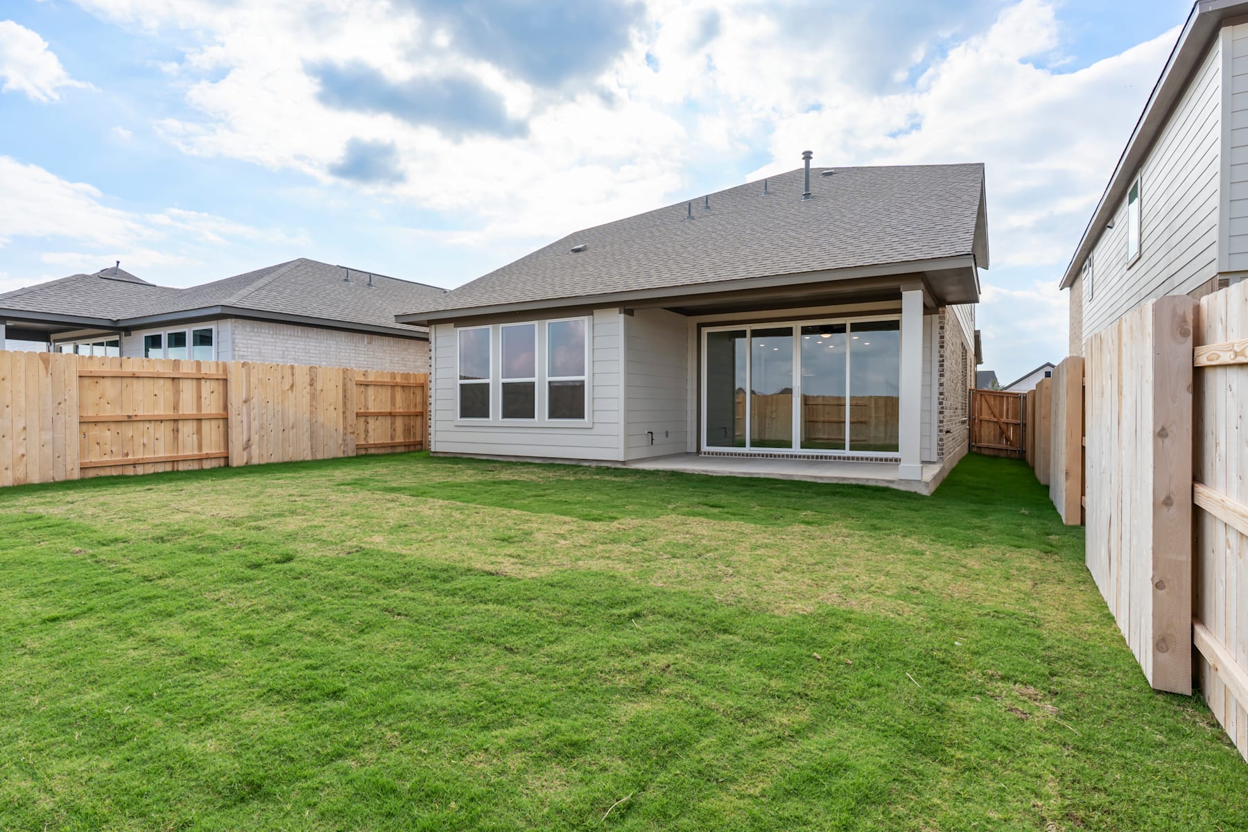 A newly constructed single-story house with a well-manicured lawn in the foreground, set against a backdrop of cloudy skies.