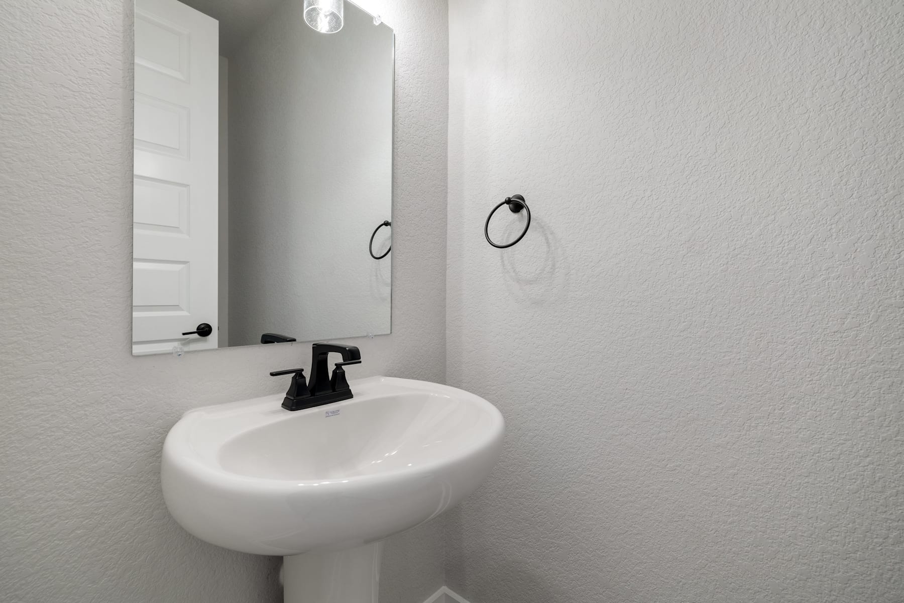 A simple, minimalist bathroom with a white pedestal sink, a mirror, and a towel ring on the wall.