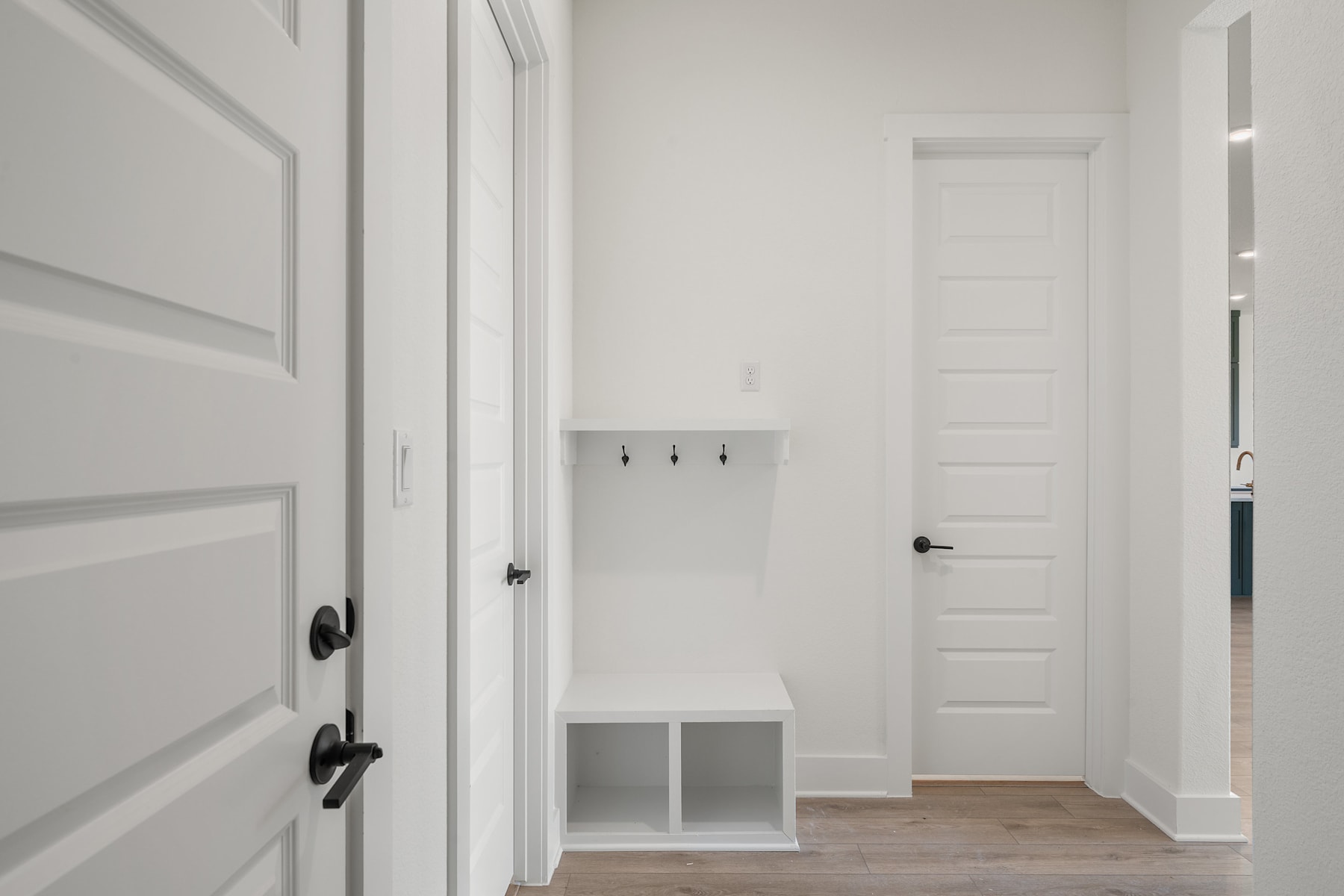 A bright, minimalist hallway with white walls, wooden flooring, and a white cabinet in the foreground.