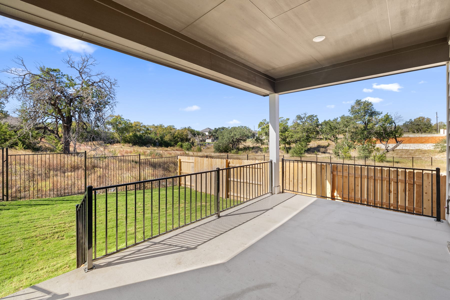 A covered patio with a metal railing overlooking a grassy yard and trees in the background.