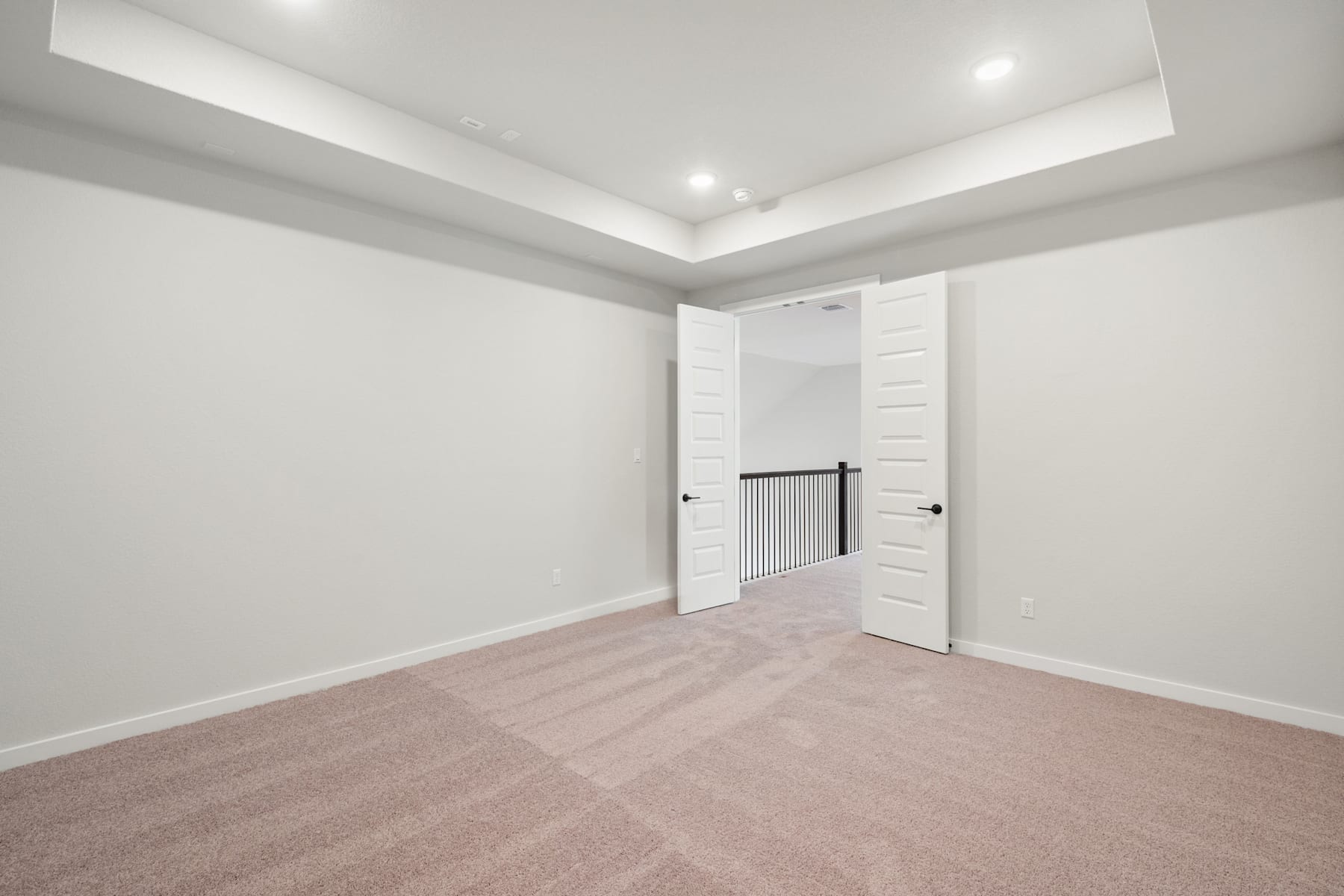 A spacious, well-lit room with white walls, a tray ceiling, and a hardwood floor. The room features a closet with white doors and a radiator on the wall.