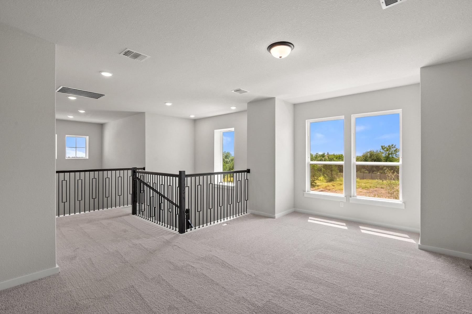 A spacious, well-lit room with a balcony overlooking a scenic outdoor landscape, featuring a carpeted floor and a metal railing.