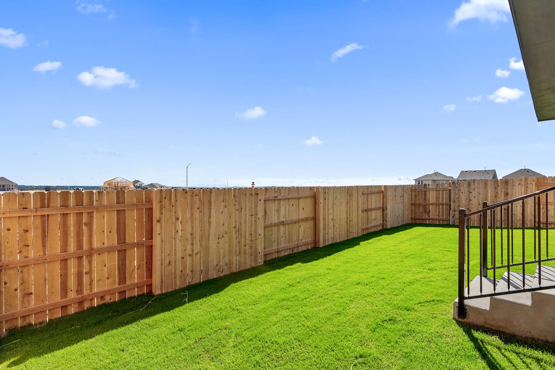 A wooden fence surrounds a lush green lawn, with a clear blue sky and scattered clouds in the background.