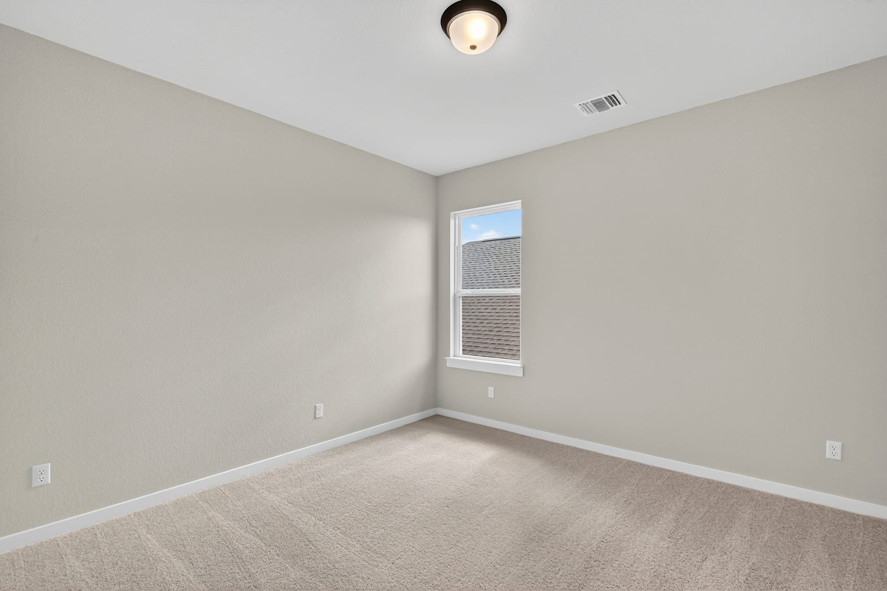 A sparsely furnished room with a small window, a light fixture, and a plain, carpeted floor.