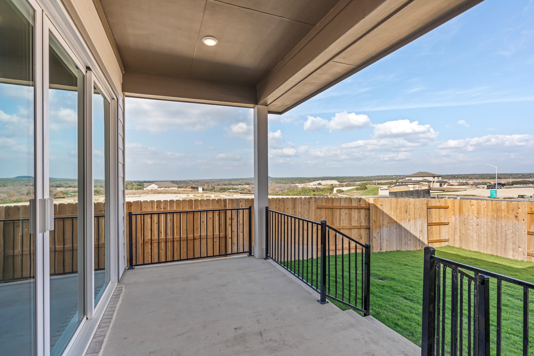 A spacious balcony with a wooden railing overlooks a grassy yard and a scenic landscape in the background, featuring a clear sky with clouds.