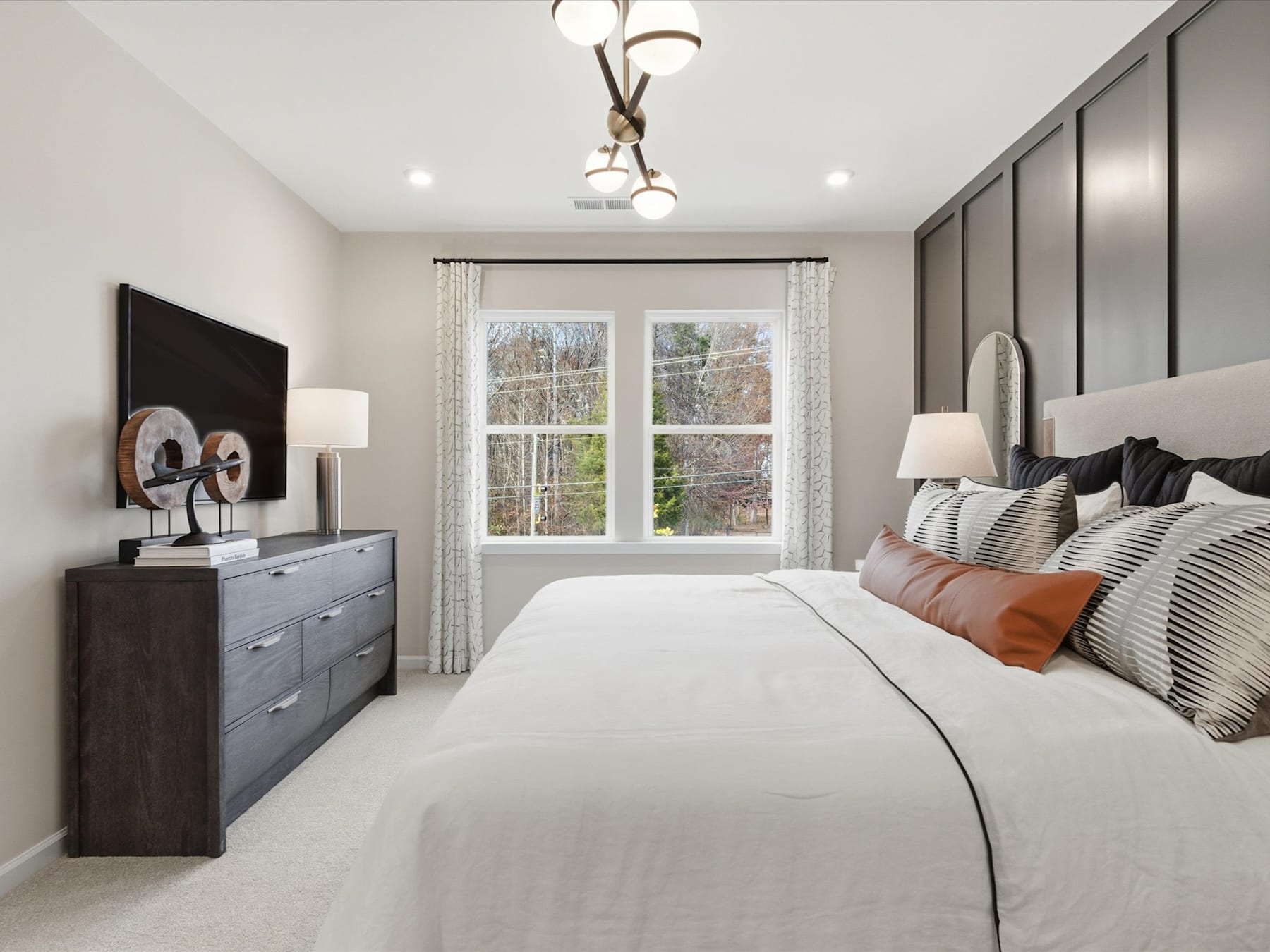 A cozy and well-designed bedroom with a large bed, dresser, and window overlooking a scenic outdoor view.