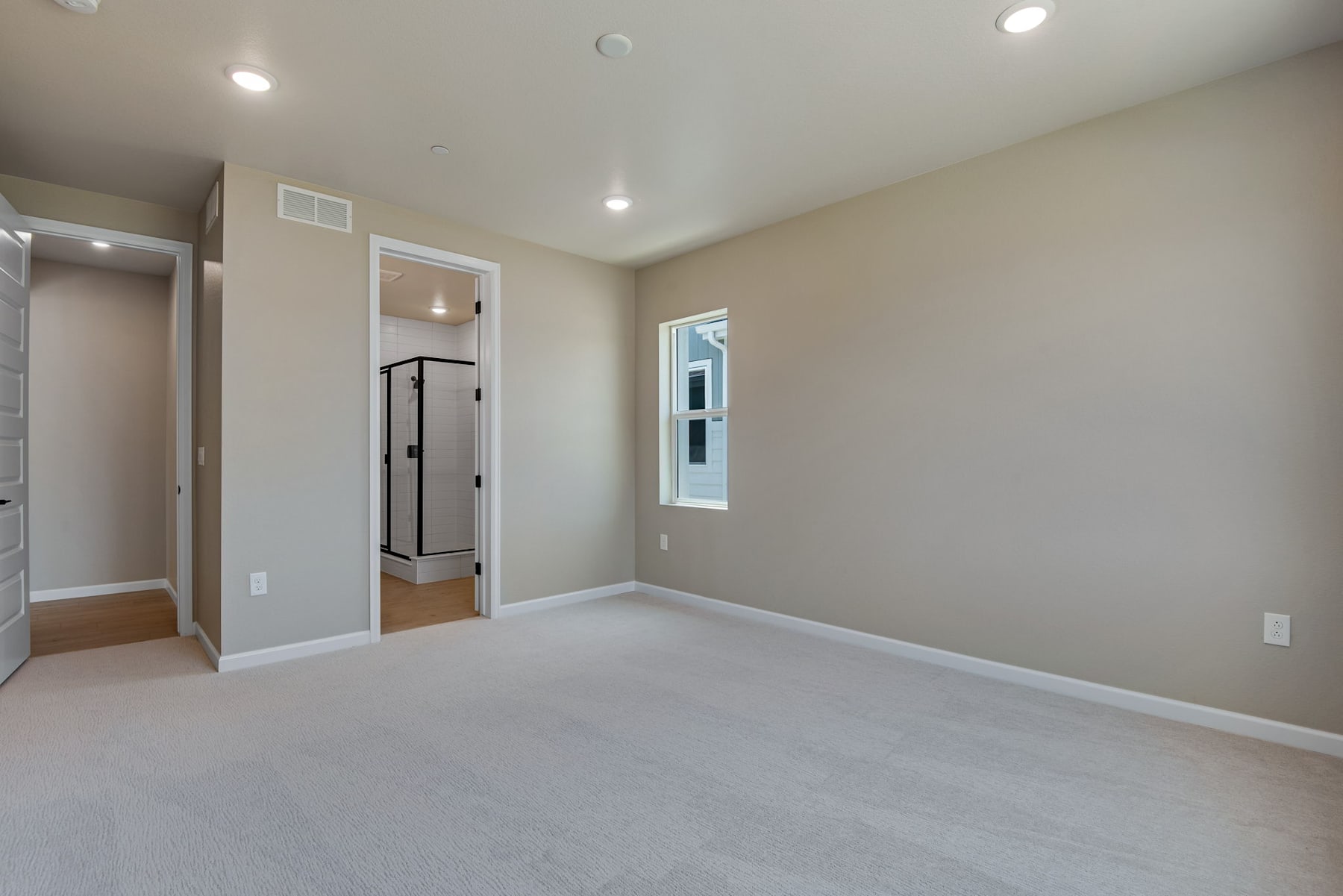 A spacious, well-lit bedroom with a neutral color scheme, featuring a closet and a window providing natural light.