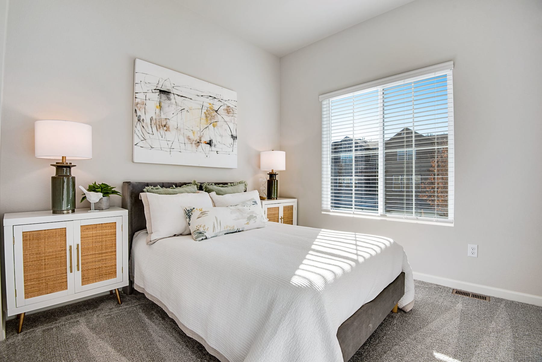 A cozy and well-designed bedroom with a large window, a white bed with decorative pillows, and a modern artwork on the wall.