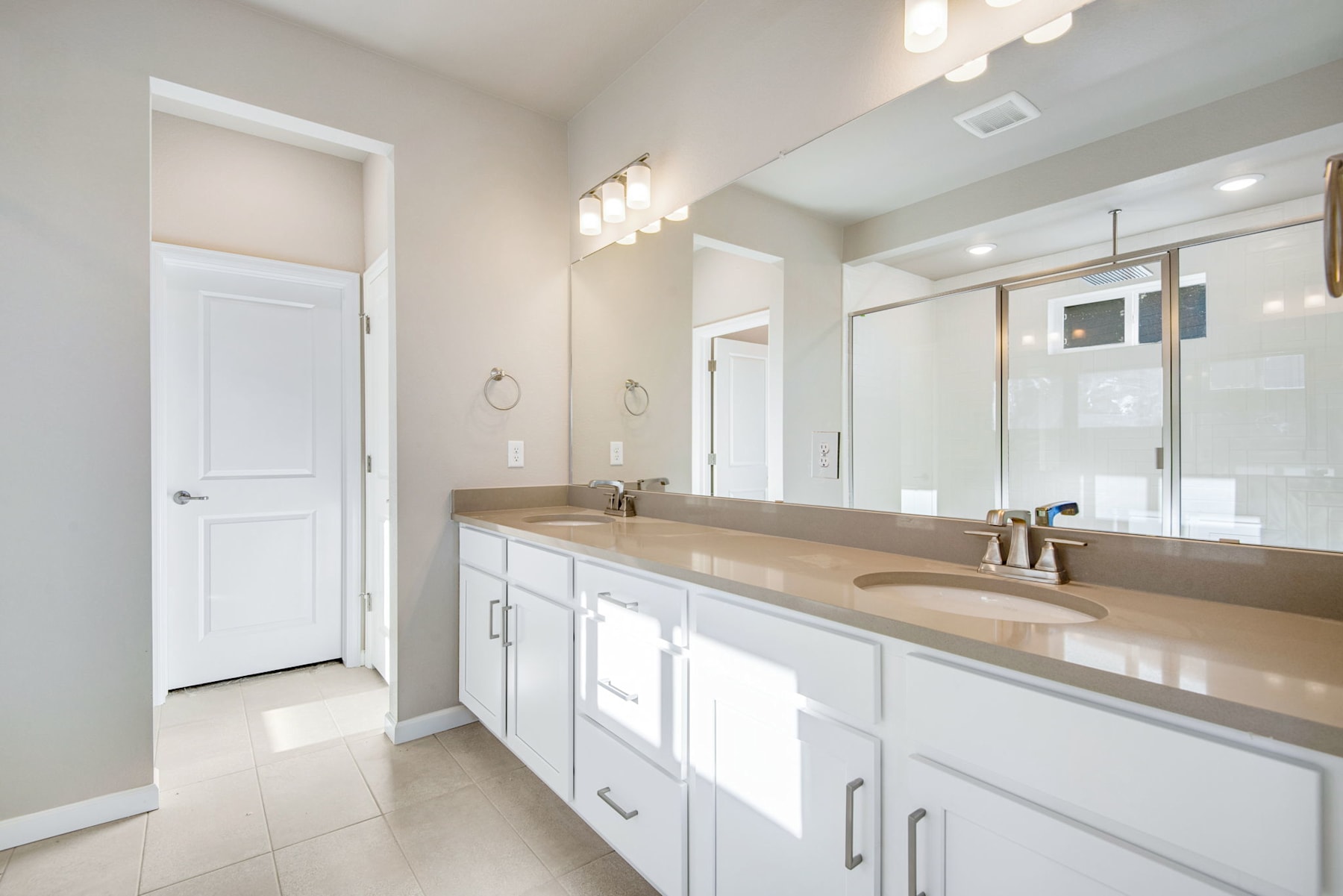 A spacious and well-lit bathroom with white cabinets, a large vanity, and a mirror taking up the majority of the wall space.
