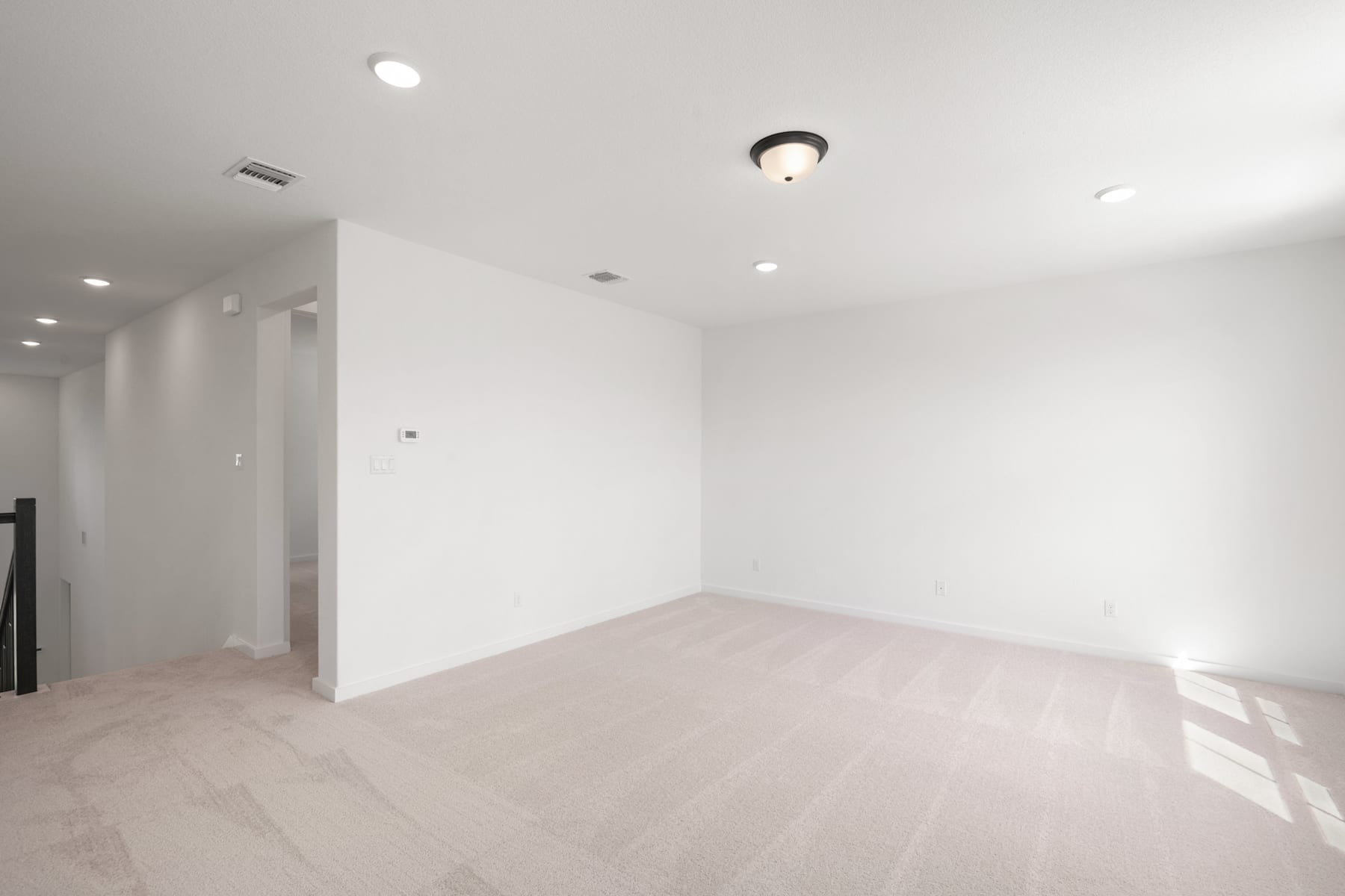 A minimalist, well-lit room with white walls, a hardwood floor, and a ceiling light fixture.