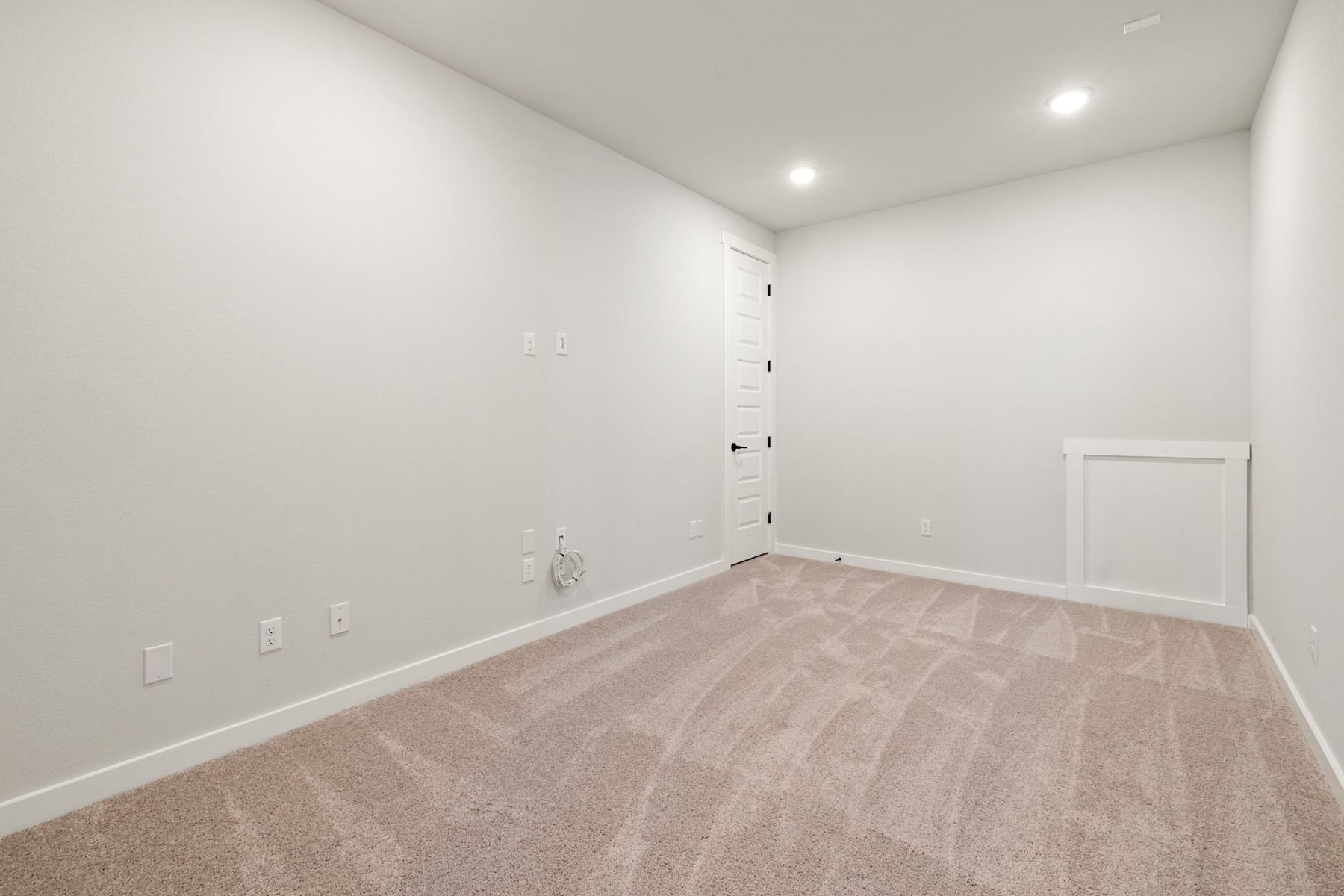 A spacious, well-lit room with white walls and a wooden floor, featuring a ladder-style shelving unit against the wall.