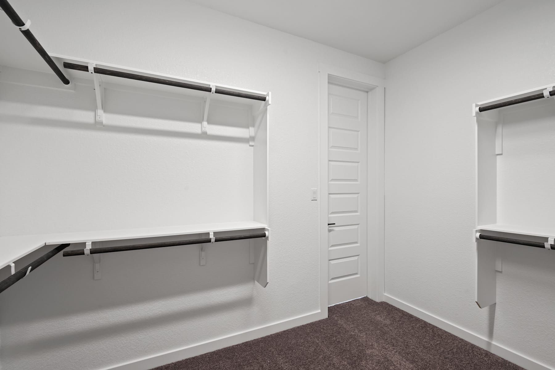 A spacious, well-lit closet with white walls, shelves, and a carpeted floor, providing ample storage space.