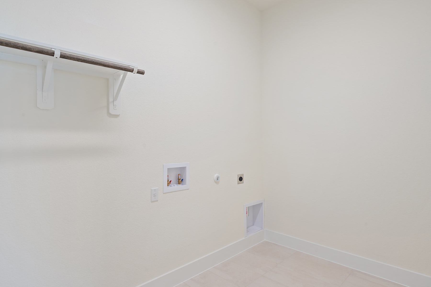 A simple, minimalist room with a white wall, a metal clothing rod, and a few electrical outlets visible.