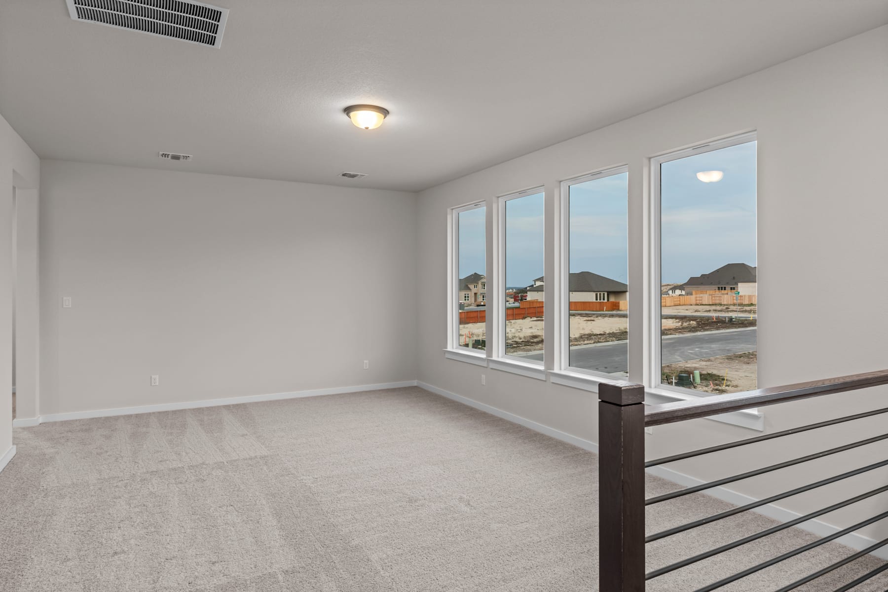 A spacious, well-lit room with large windows overlooking a residential neighborhood in the background.
