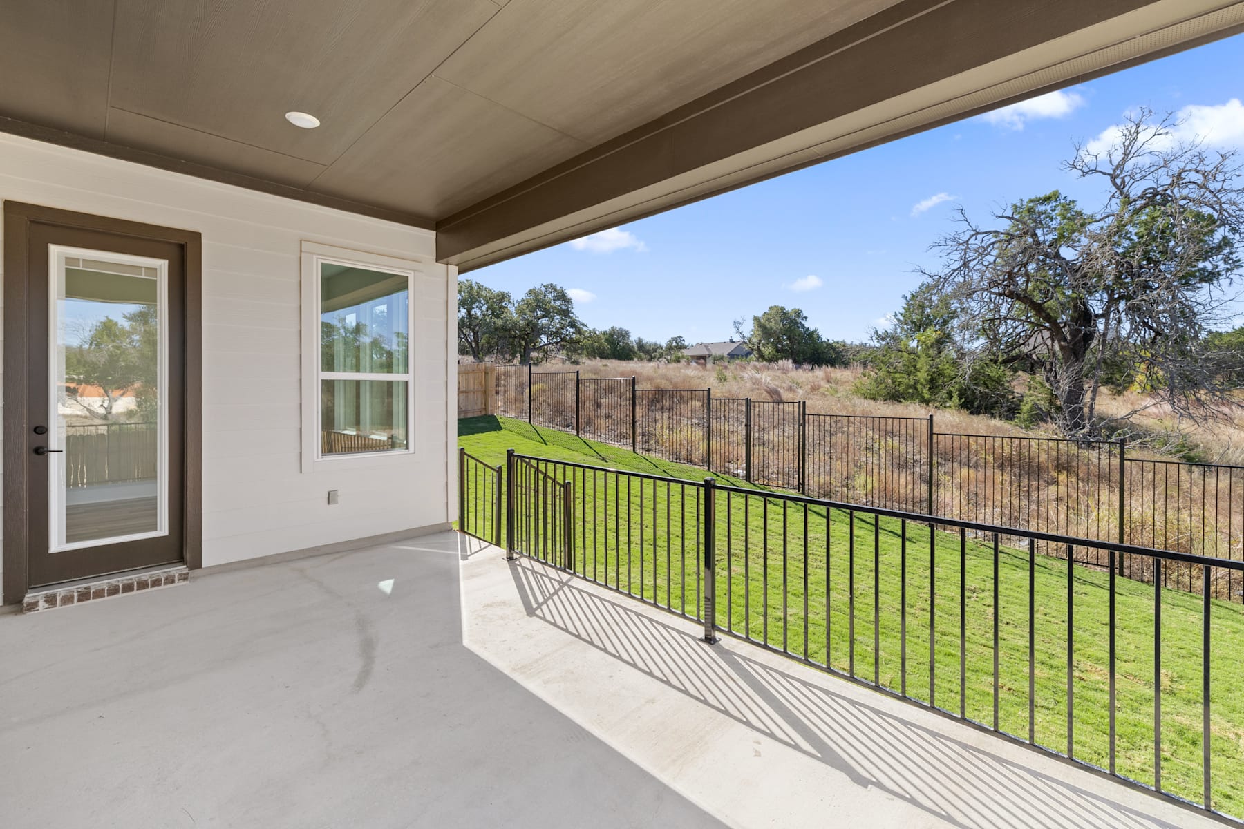 A spacious patio with a metal railing overlooks a lush, grassy landscape surrounded by trees in the background.