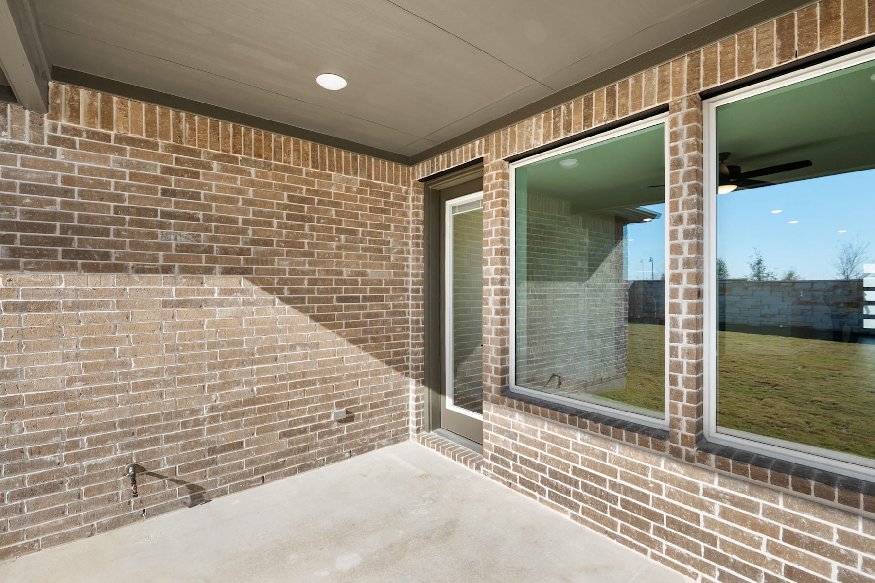 The image shows a covered porch with a brick wall and large windows, providing a view of the outdoor landscape.