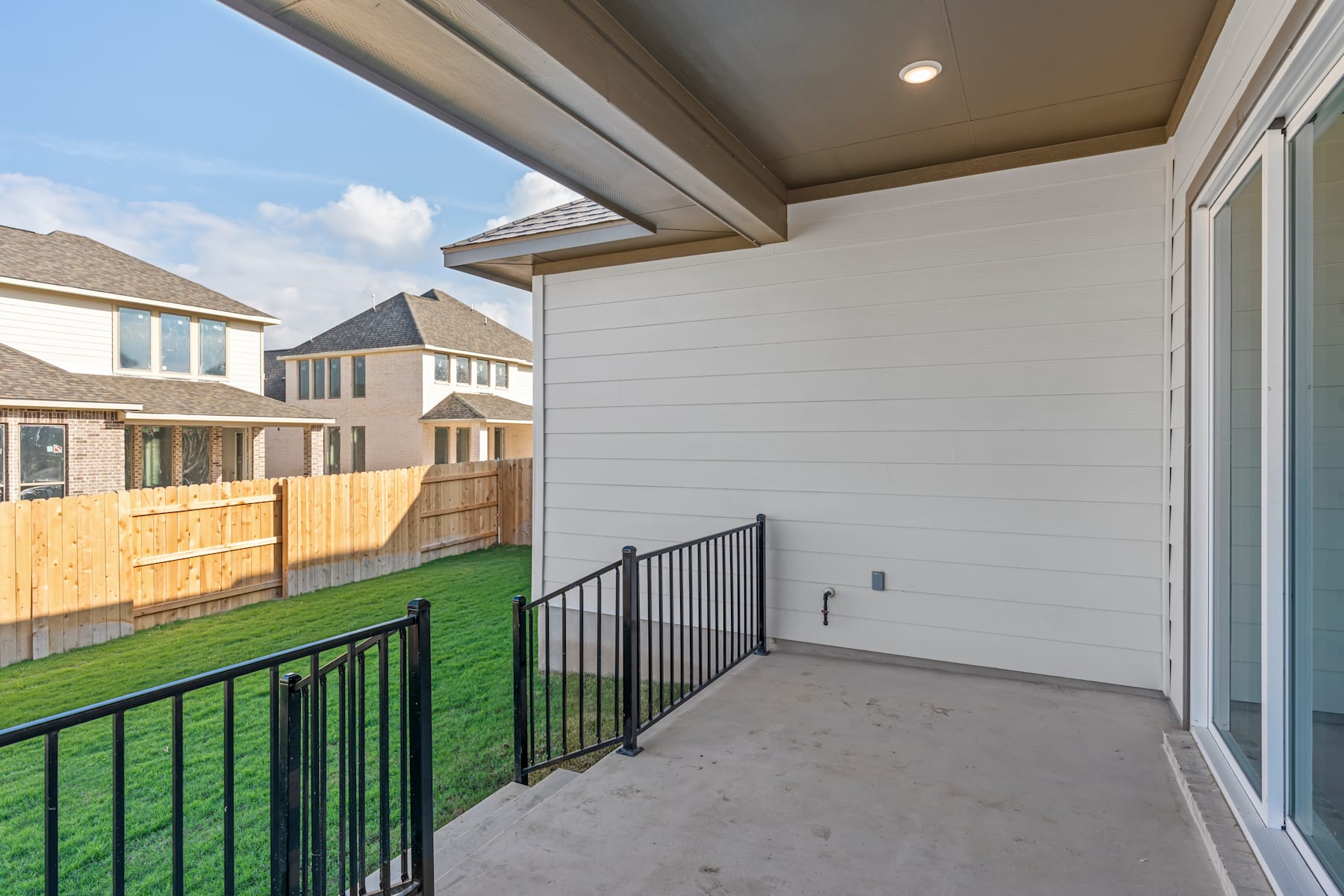 A covered patio with a metal railing overlooking a grassy backyard and neighboring houses in the background.