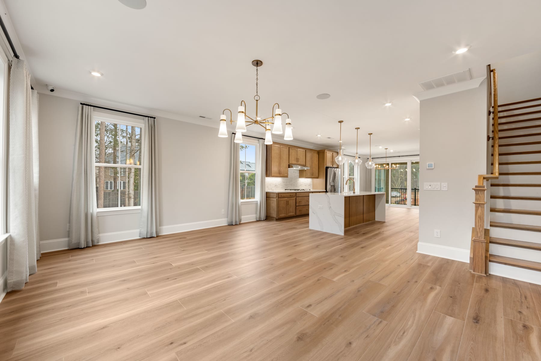A spacious and modern open-plan living area with hardwood floors, a kitchen with wooden cabinets, and a staircase leading to an upper level.
