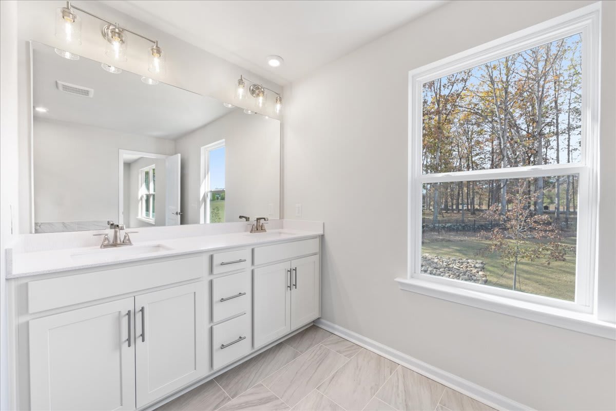 A spacious and well-lit bathroom with a large vanity, a mirror, and a window overlooking a wooded outdoor scene.
