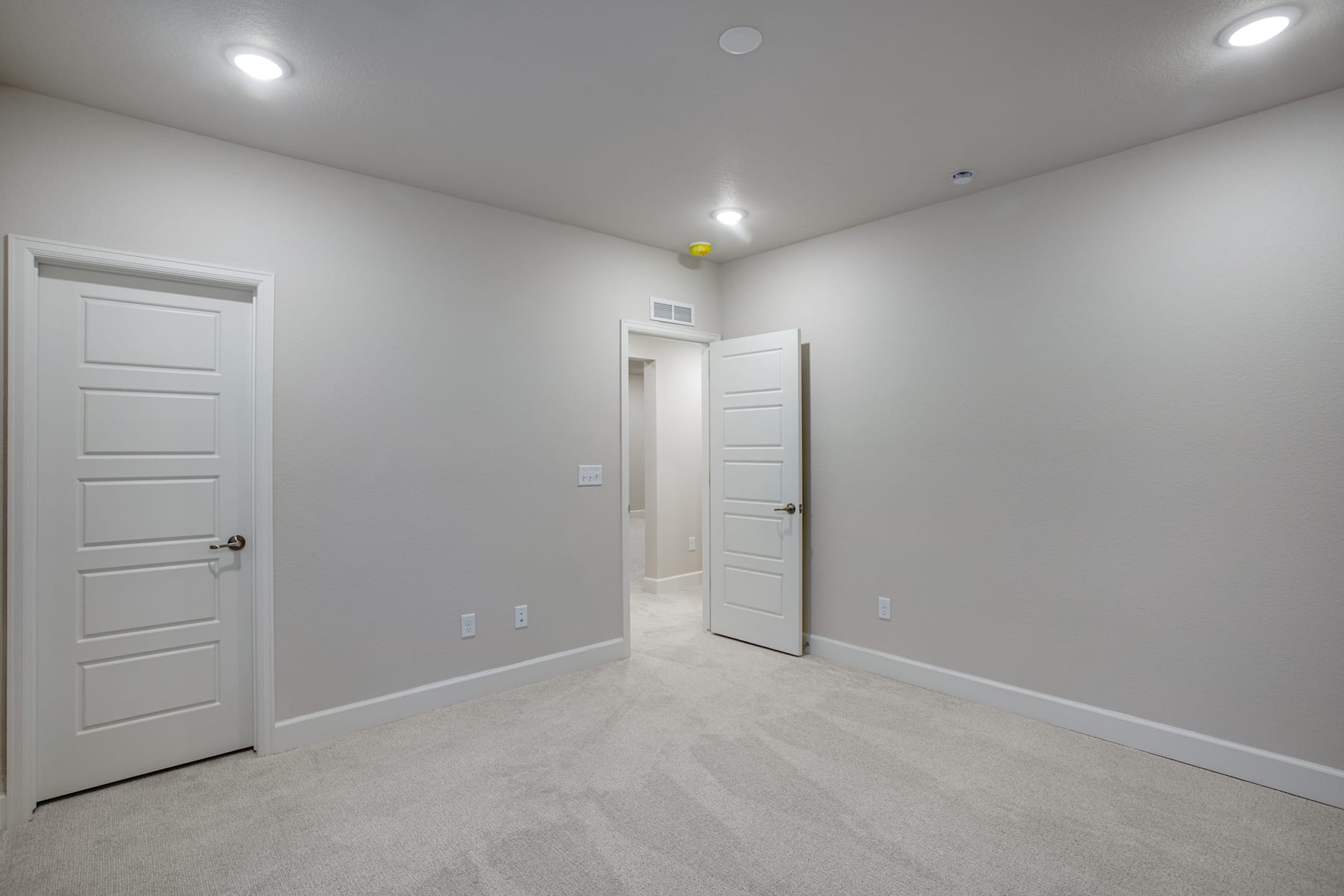 A spacious, minimalist room with white walls, doors, and a light-colored floor, creating a clean and bright atmosphere.