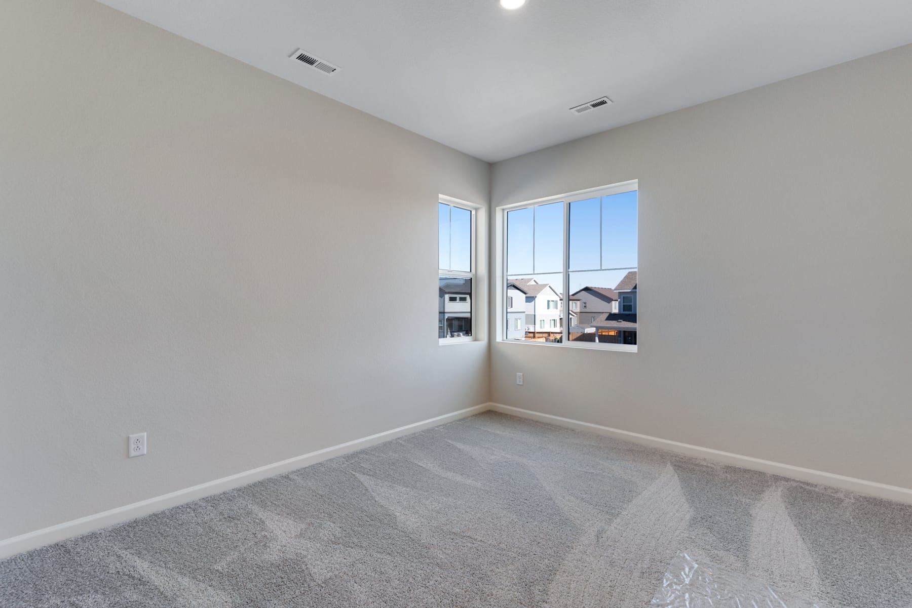 A spacious, well-lit room with a large window overlooking a residential neighborhood, featuring a clean, minimalist design with gray carpeting and neutral-toned walls.