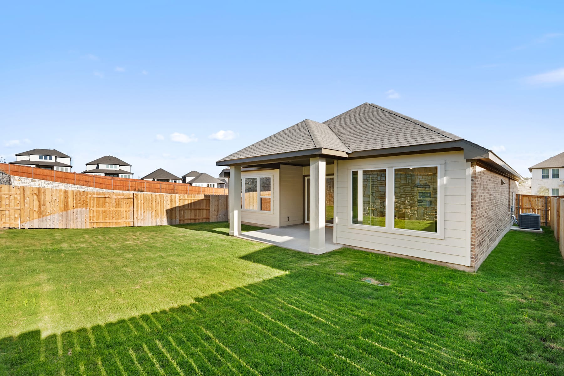 A well-manicured lawn surrounds a modern, single-story house with a peaked roof and large windows, set against a clear blue sky with a few clouds.