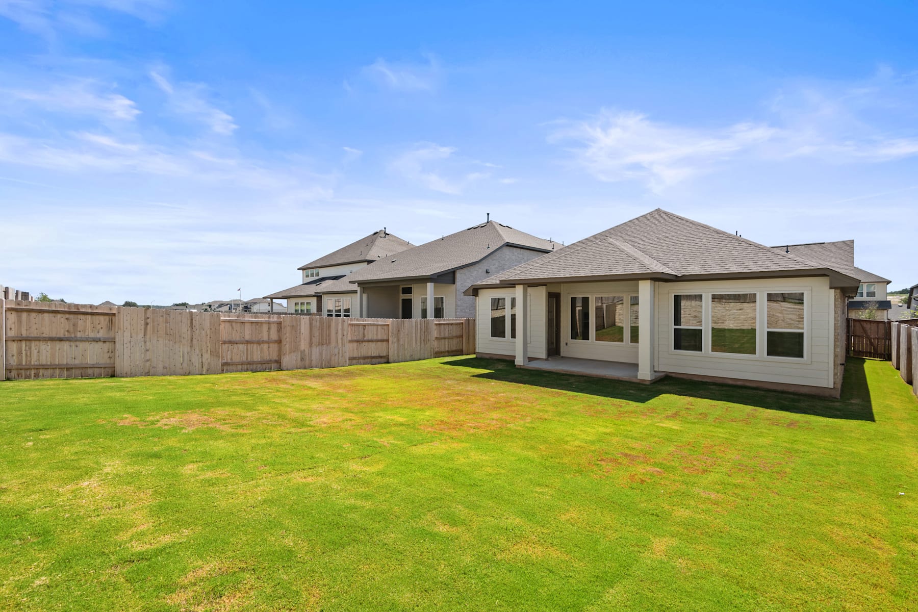 A large, modern house with a spacious yard covered in lush green grass, set against a clear blue sky with scattered clouds.