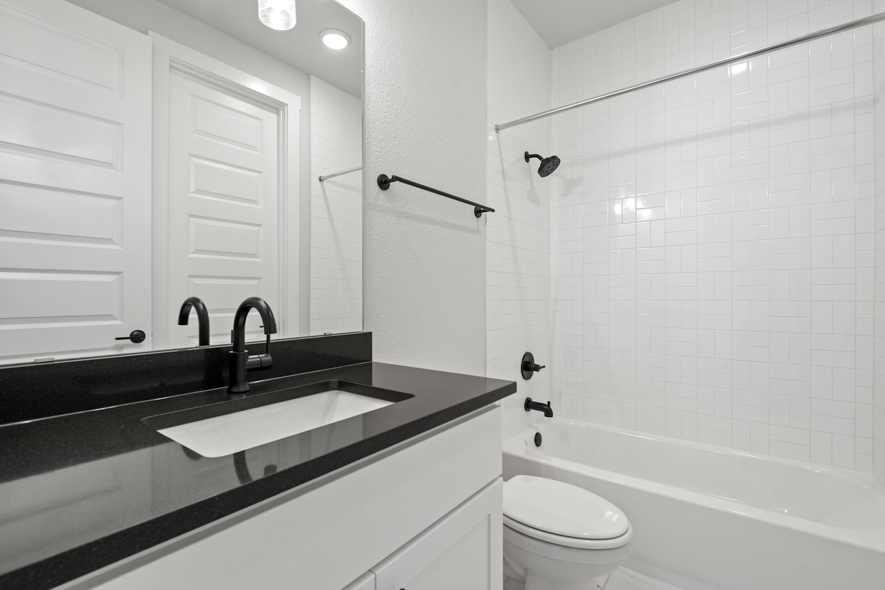 A modern, minimalist bathroom with a white vanity, black countertop, and a bathtub in the background.
