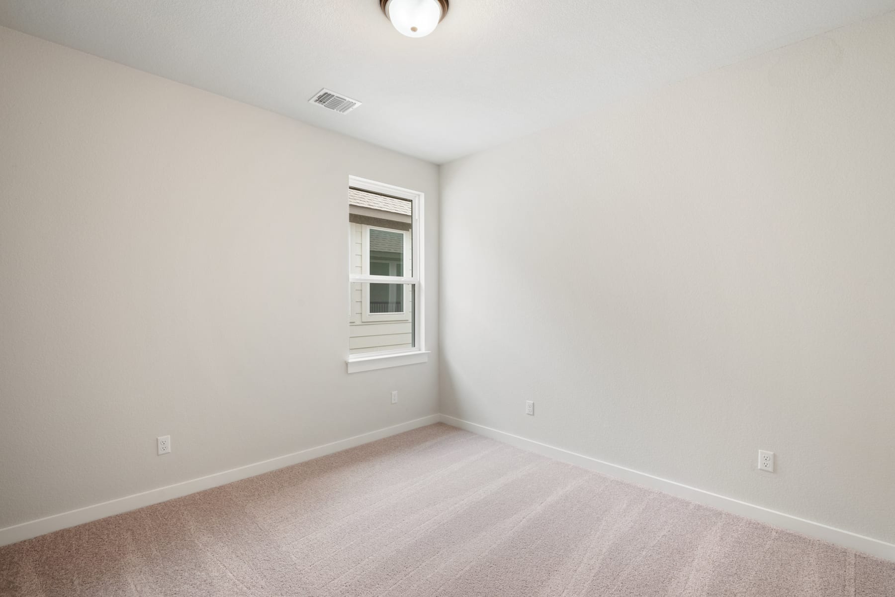 A simple, minimalist bedroom with a single window, a light fixture, and a hardwood floor.